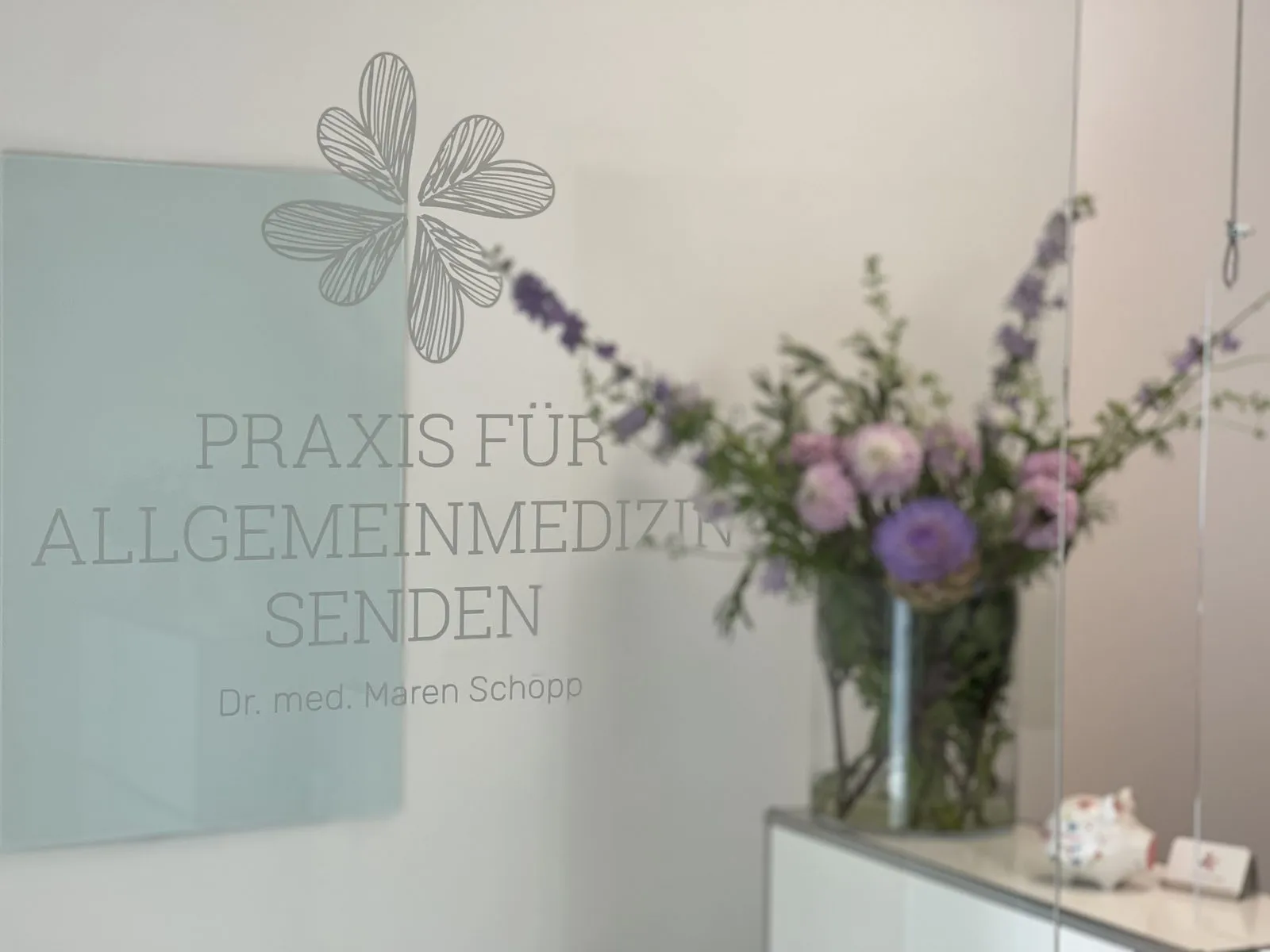 Empfangsbereich der Praxis mit Praxislogo und Blumenstrauß
